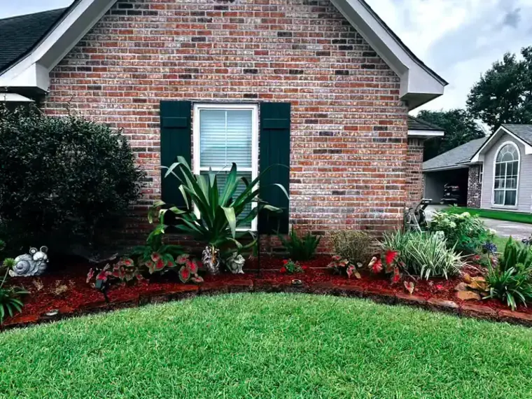 Curved flower bed with red brick edging, red mulch and fresh plantings in front of a brick house
