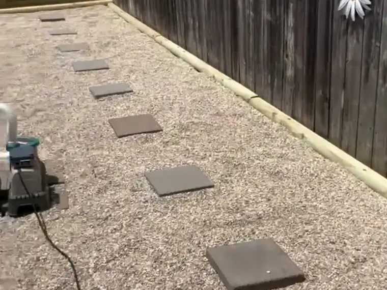 Gravel walkway with square stepping stones laid along a wooden fence
