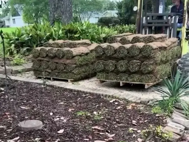 Pallets of fresh sod rolls stacked beside a brick-edged bed, ready to lay