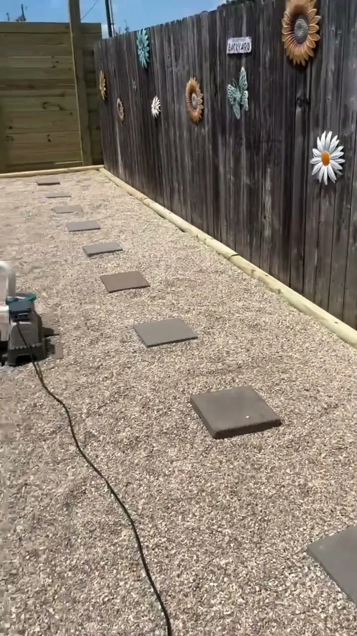 Gravel walkway with square stepping stones laid along a wooden fence