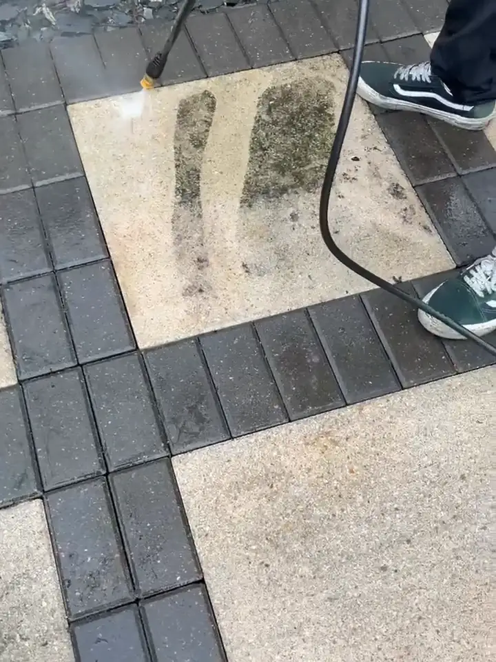 Pressure washer cutting a clean stripe through a grimy paver